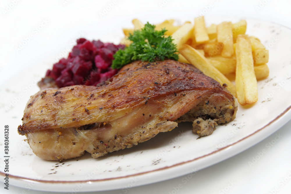 Roasted chicken quarter leg with crispy golden brown skin, baked potatoes and beet salad on white plate. Food background.