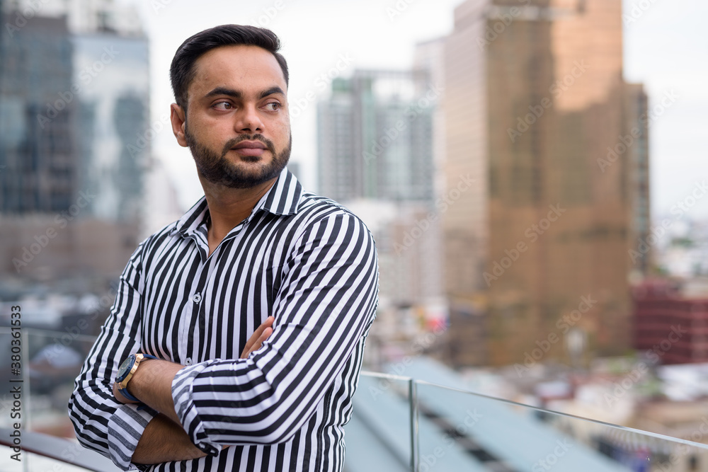 Obraz premium Young bearded Indian businessman against view of the city