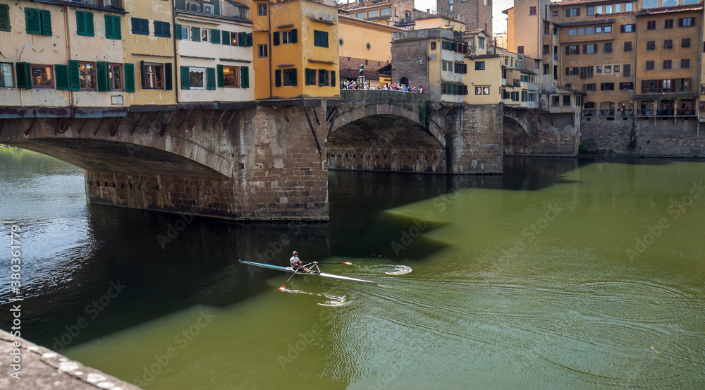 Florence, Italy: Ponte Vecchio over the Arno river on a sunny day; a rowing boat is going under the bridge