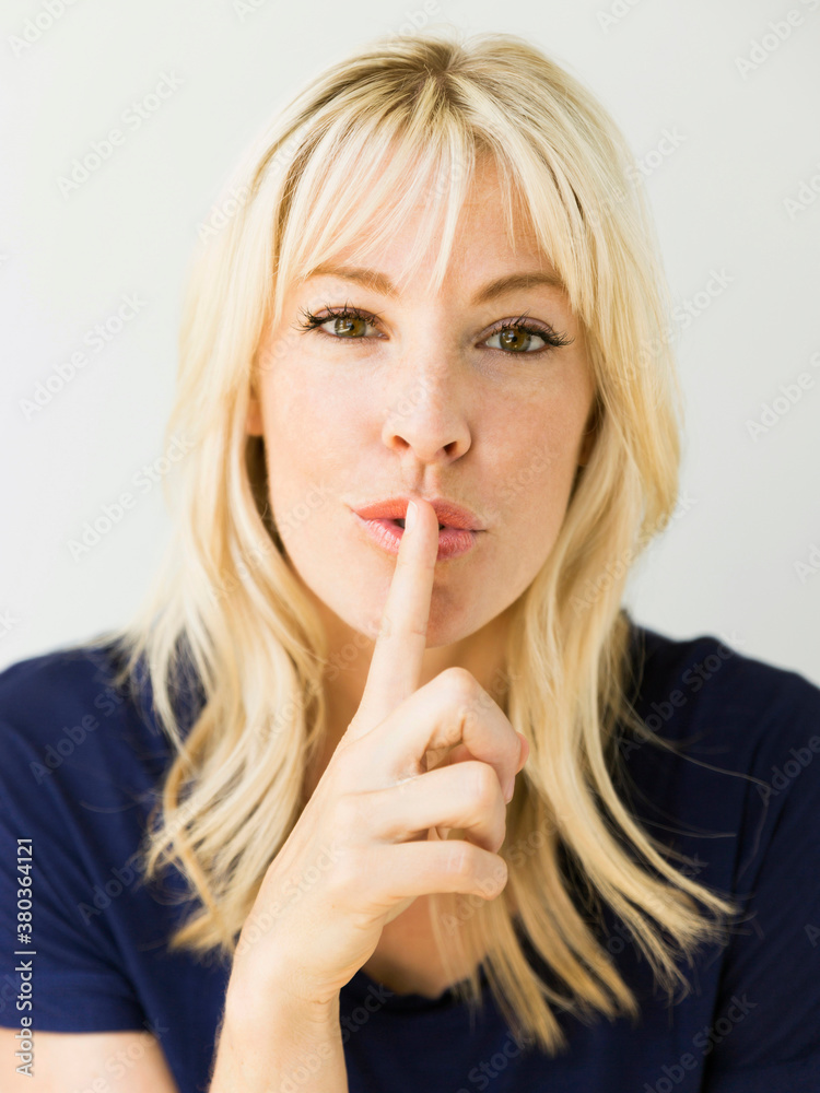 Studio portrait of blonde woman with finger on lips Studio portrait of blonde woman with finger on lips