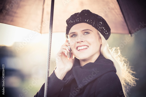 Smiling woman under umbrella using mobile phone photo