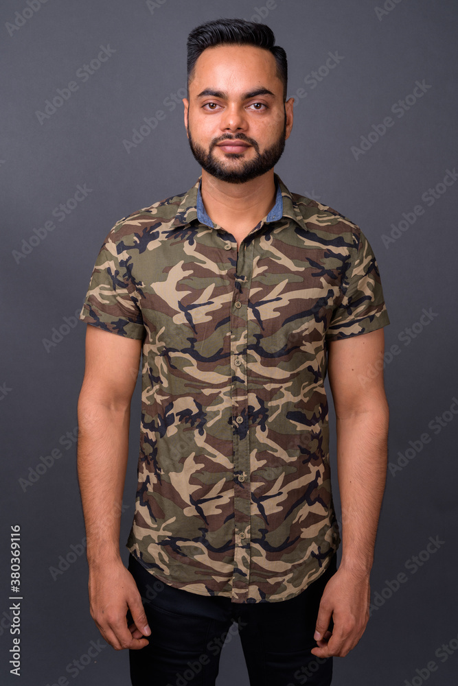 Young bearded Indian man against gray background