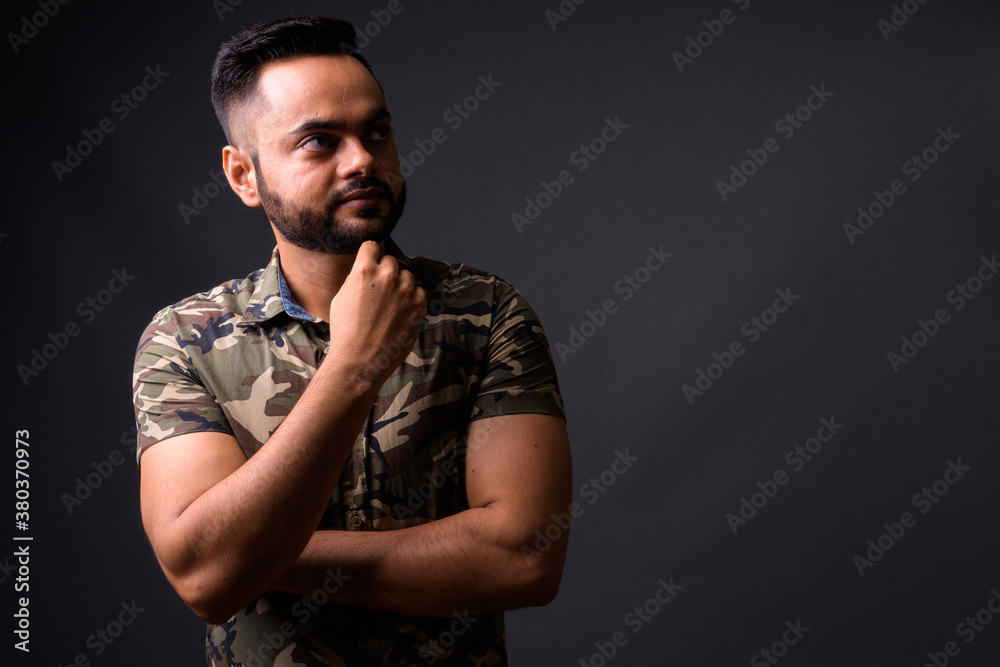 Young bearded Indian man against gray background