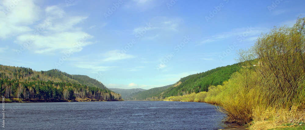A wide river runs slowly towards the wooded mountains.