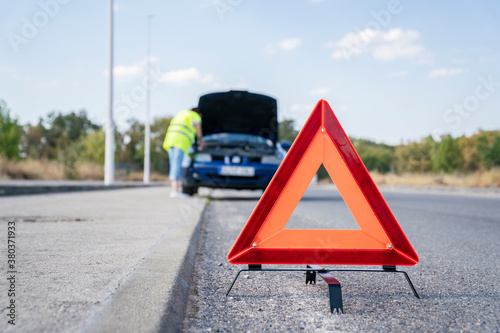 Road breakdown signaling triangle with broken down car in the background