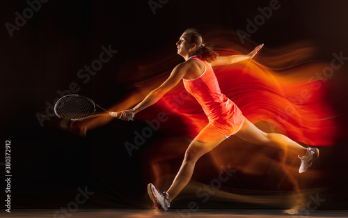 Champion. Professional female tennis player training isolated on black studio background in mixed light. Woman in sportsuit practicing. Healthy lifestyle, sport, workout, motion and action concept.