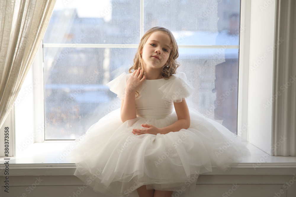 a beautiful little girl in a white dress is waiting for Santa Claus at the window. children's fairy tales and dreams. happy childhood. festive smart clothes. a beautiful little girl in a white dress is waiting for Santa Claus at the window. children's fairy tales and dreams. happy childhood. festive smart clothes.