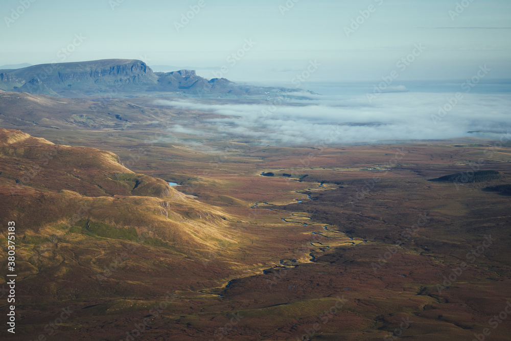 A top view of an autumn mountain valley with winding river and the sea covered with low clouds at dawn. The Isle of Skye, Scotland, UK