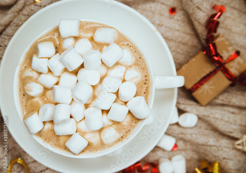 Coffee with marshmallows on a background of knitted fabric with gifts and holiday bows.Hot winter drink.