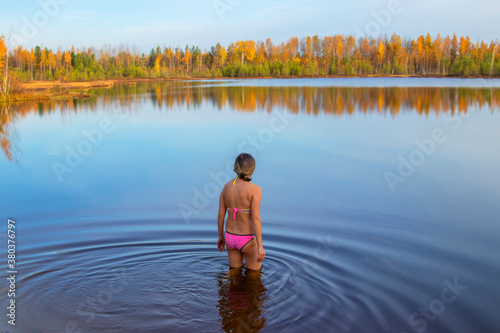 A woman in a pink bathing suit enters the bathing lake.