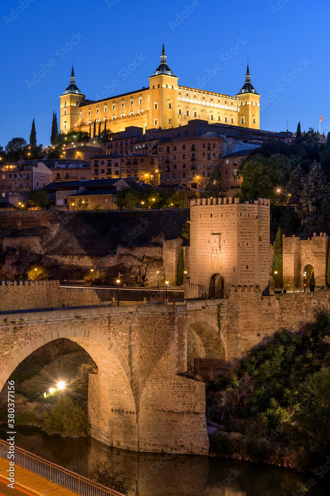 Toledo at Dusk - A vertical dusk view of the historic city Toledo at Puente de Alcántara - an ancient Roman arch bridge located in front of eastern city gate Puerta de Alcántara. Toledo, Spain.