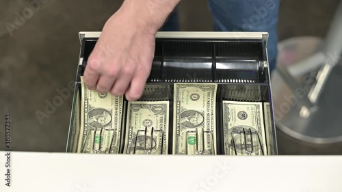 The seller takes dollars from the cash register in the store, close-up