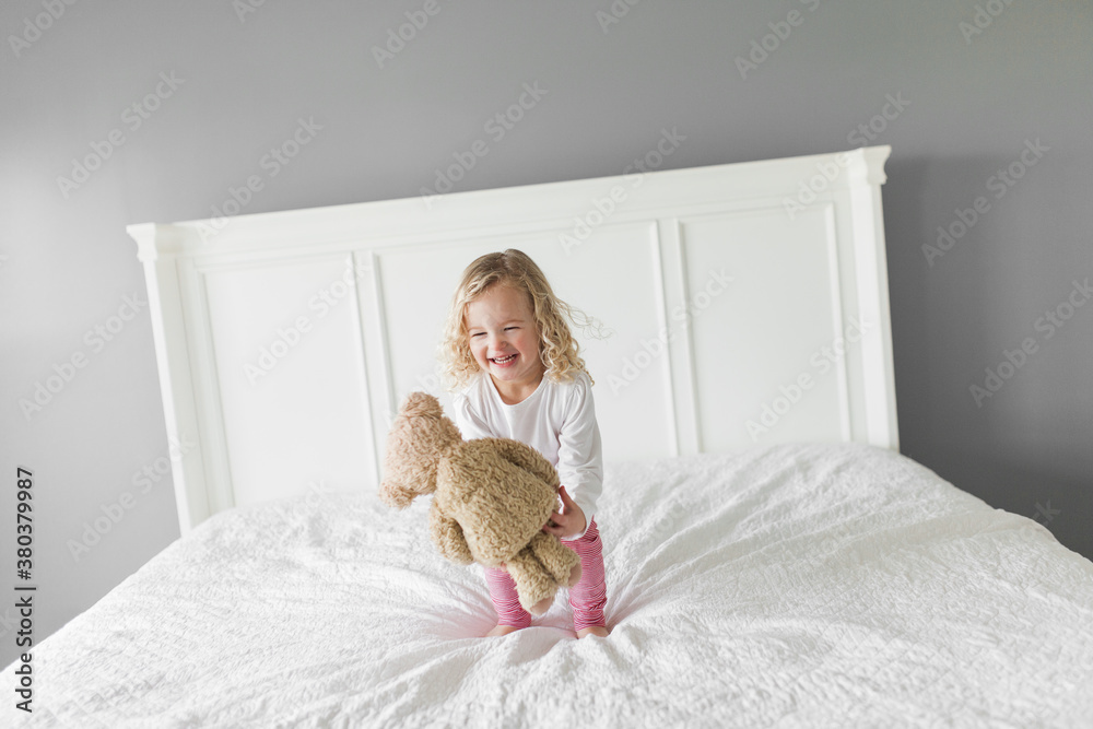 Laughing young girl wearing red and white striped pajamas catches teddy bear Laughing young girl wearing red and white striped pajamas catches teddy bear