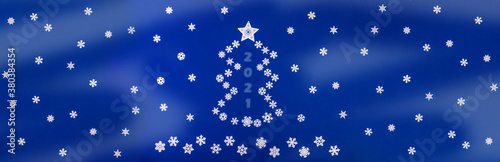 Festive wide banner - Xmas symbol - Christmas tree laid out from snowflakes on blue background with copy space for text.