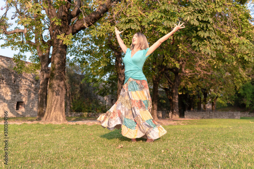 Beautiful barefoot girl in a long colorful skirt is dancing in natural background