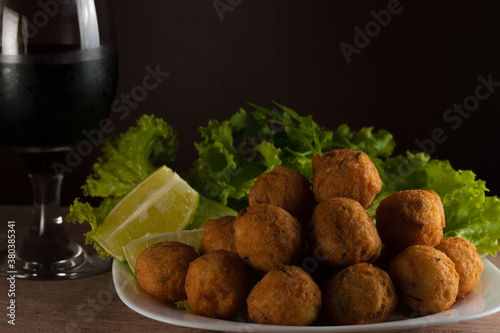 Salt cod fritters in a white plate with fresh lemons,salad and wine cup. Selective focus. Copy space