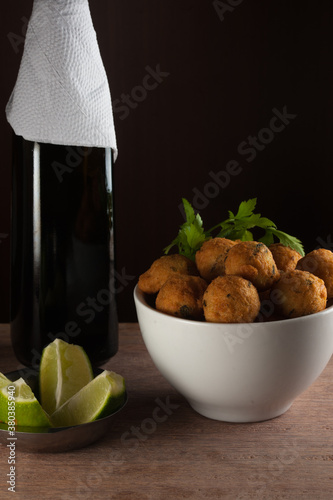 Salt cod fritters in a white bowl with chopped lemons and olive oil bottle. Copy space. Selective focus