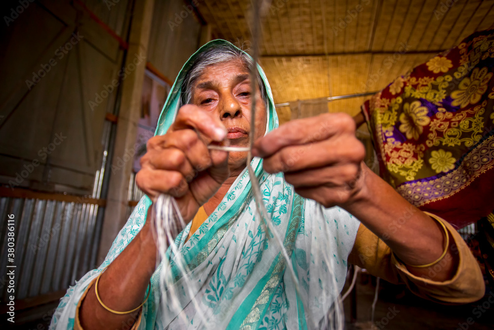 Fototapeta premium An old age woman is making on his skinny hands a rope from the banana tree fiber at Madhupur, Tangail, Bangladesh.