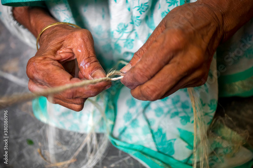An old age woman is making on his skinny hands a rope from the banana tree fiber at Madhupur, Tangail, Bangladesh.