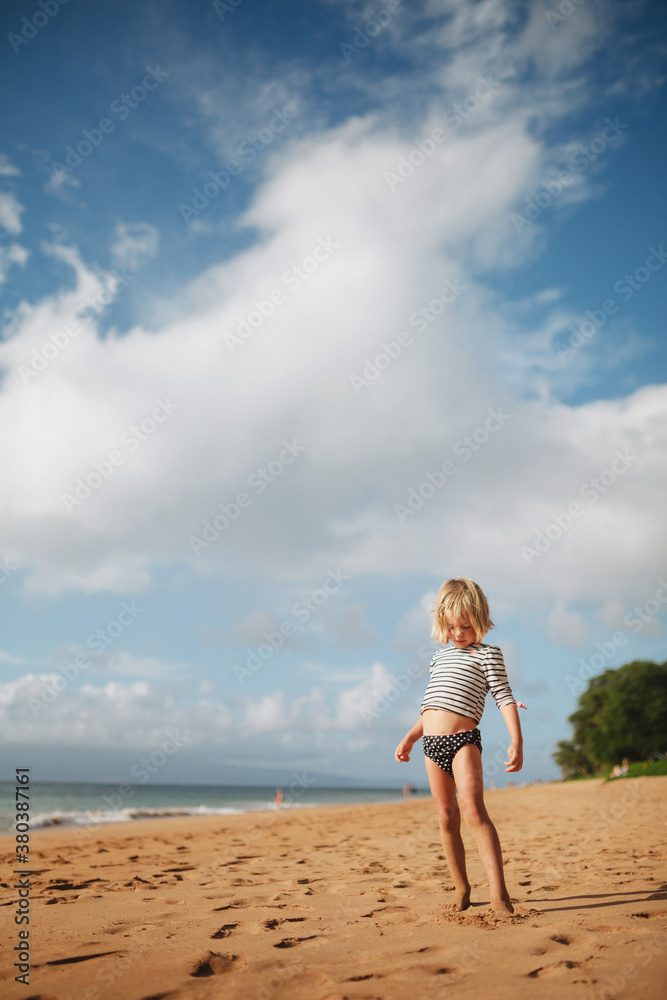 Cute young girl looking at belly on sandy tropical beach in summer Cute young girl looking at belly on sandy tropical beach in summer