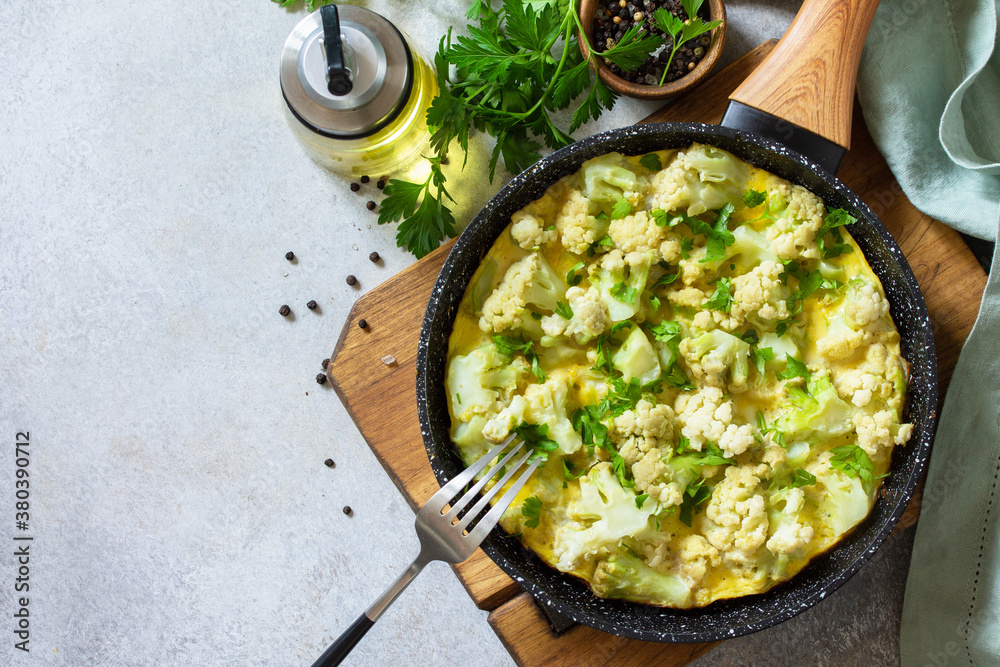 Healthy breakfast or diet lunch. Egg omelet with cauliflower in a cast-iron pan on a light stone table top. Flat lay top view. Copy space. Healthy breakfast or diet lunch. Egg omelet with cauliflower in a cast-iron pan on a light stone table top. Flat lay top view. Copy space.