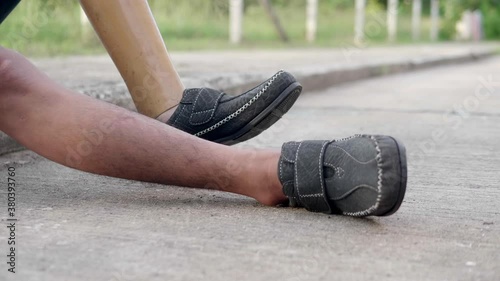 Slow motion of a poor disabled man  wearing a left prosthetic leg and a disabled left arm is sitting on the sidewalk on the roadside.