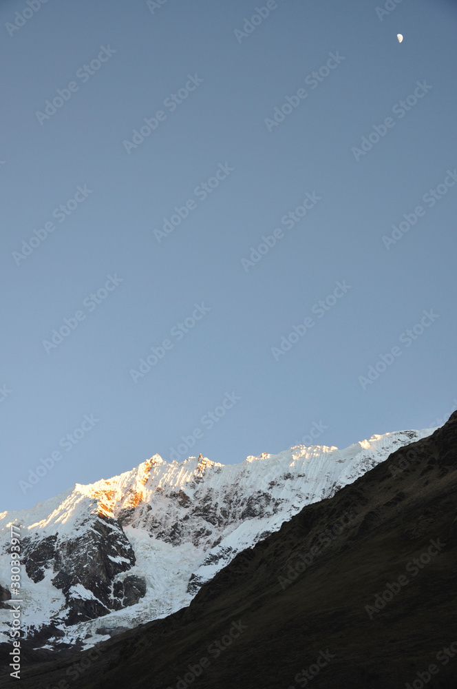 Snow capped mountains in the Andes range of Peru, as seen in the early evening with the moon high in the sky