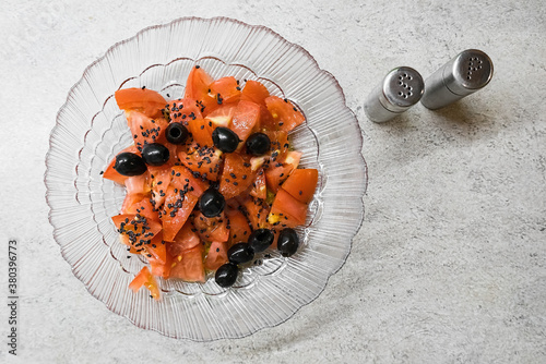 Vegetarian salad with tomato, olives and black sesame seeds. Salad on the kitchen table.