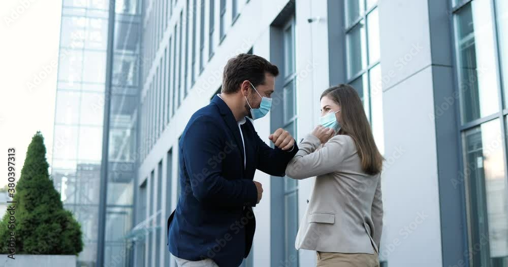 Caucasian young joyful female and male in medical masks meeting at street and greeting with elbows. Happy businessman and businesswoman talking and chatting cheerfully. Couple of friends. Caucasian young joyful female and male in medical masks meeting at street and greeting with elbows. Happy businessman and businesswoman talking and chatting cheerfully. Couple of friends.