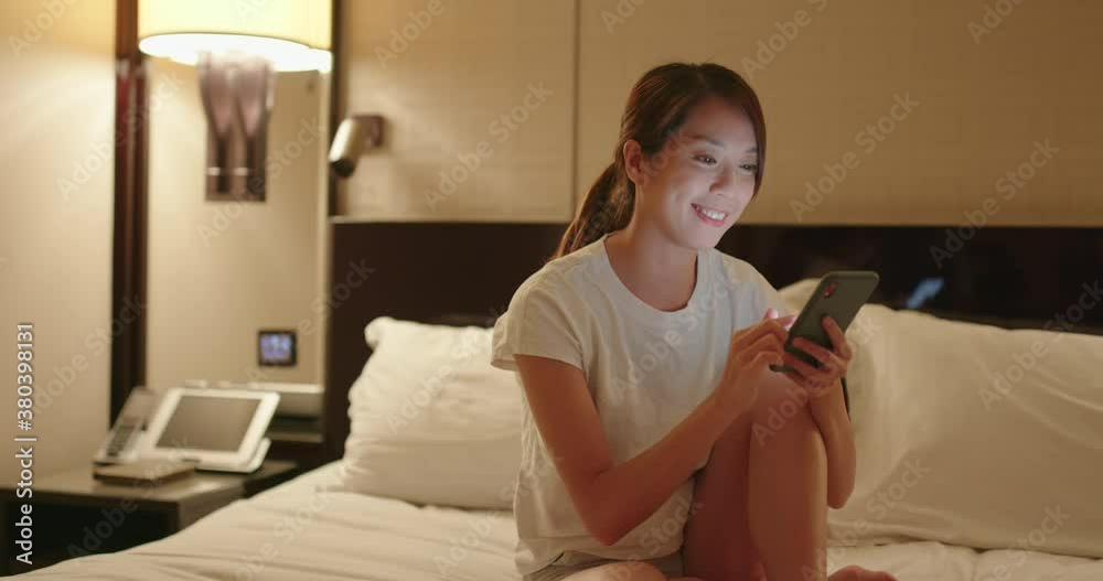 Woman use of mobile phone and sit on bed at night Woman use of mobile phone and sit on bed at night