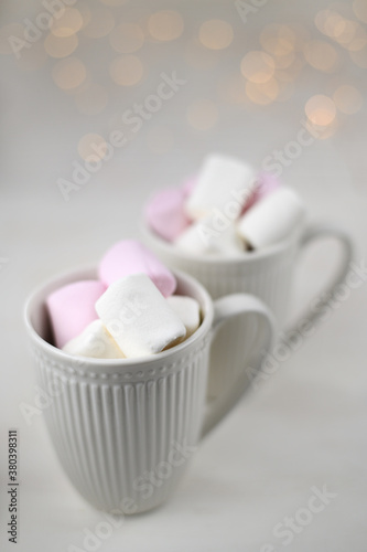 Hot winter drink with cocoa and marshmallows in mugs on wooden white background with Christmas garland. Top view.