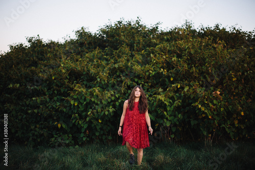 Young woman emerges from the bushes wearing a red dress