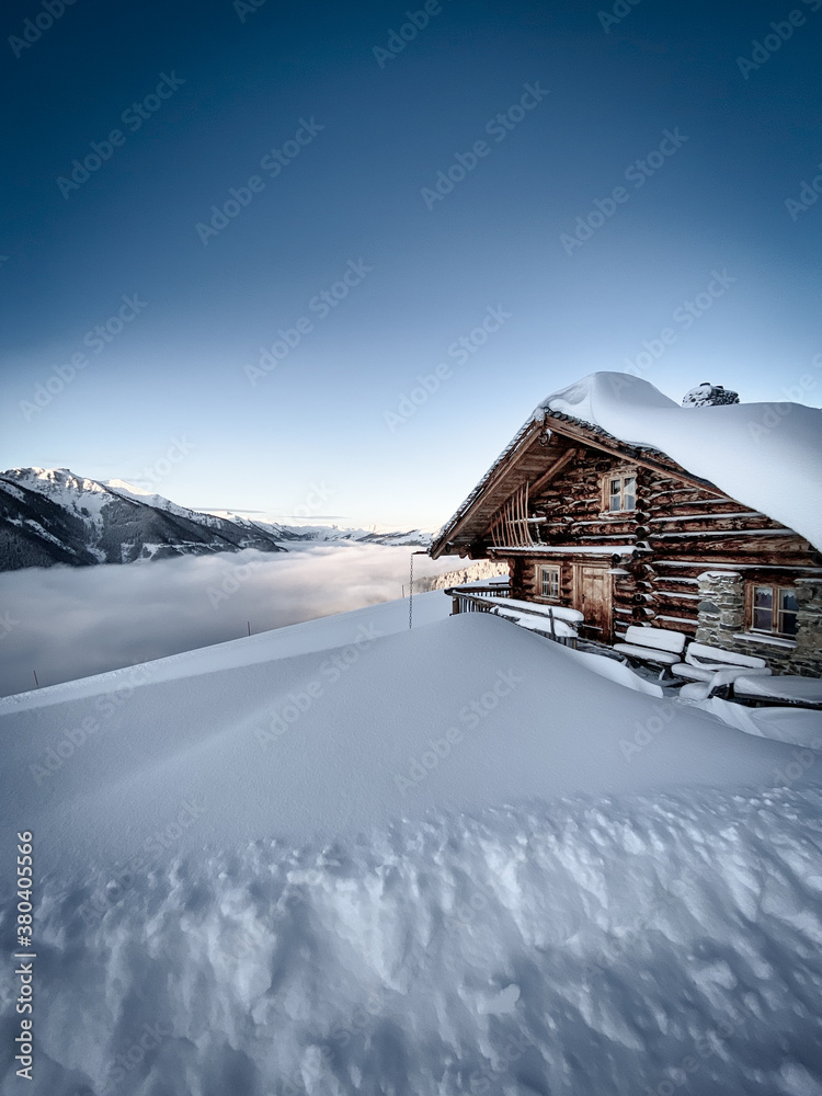Snow covered mountain hut old farmhouse in the Austrian alps at sunrise against blue sky.