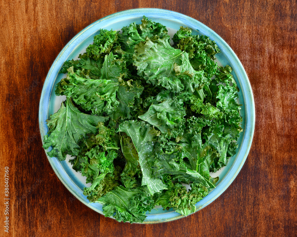 Plate of homemade kale chips on a rustic wood table Plate of homemade kale chips on a rustic wood table