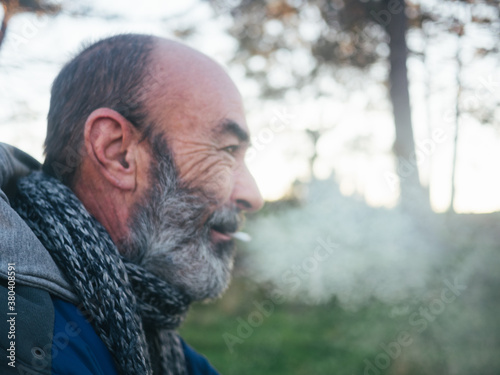 Old bearded man smoking a cigarette outside