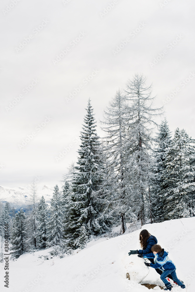 Girl and a boy making a huge snowball, first step to make a snowman Girl and a boy making a huge snowball, first step to make a snowman