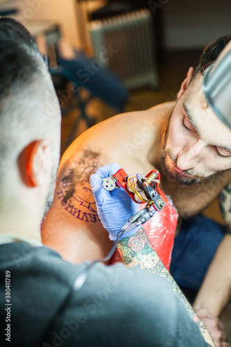 Tattoo artist working on tatoo on mans's shoulder. photo