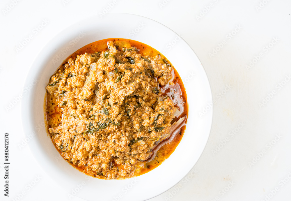 Egusi soup with beef in a white plate on a white background with negative space. Flatlay view Egusi soup with beef in a white plate on a white background with negative space. Flatlay view