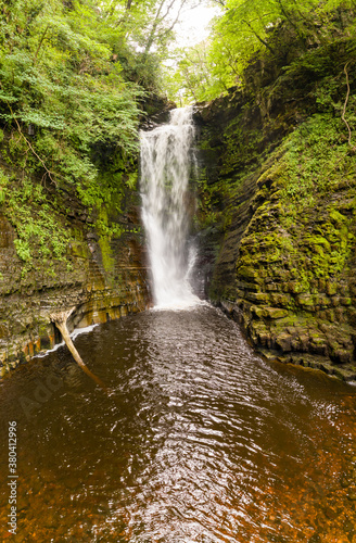 Fototapeta Naklejka Na Ścianę i Meble -  Tall waterfall in a narrow canyon surrounded by green foliage (Sgwd Einion Gam, Waterfall Country, Wales)