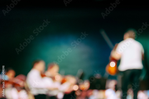 A conductor holding a violin leads a string orchestra, intentionally blurred photo