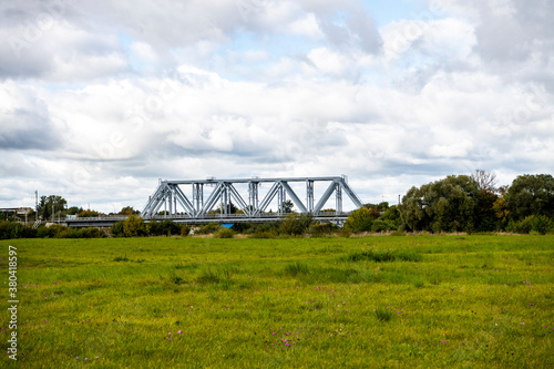 railway bridge over the river against the background of green meadow and gray clouds