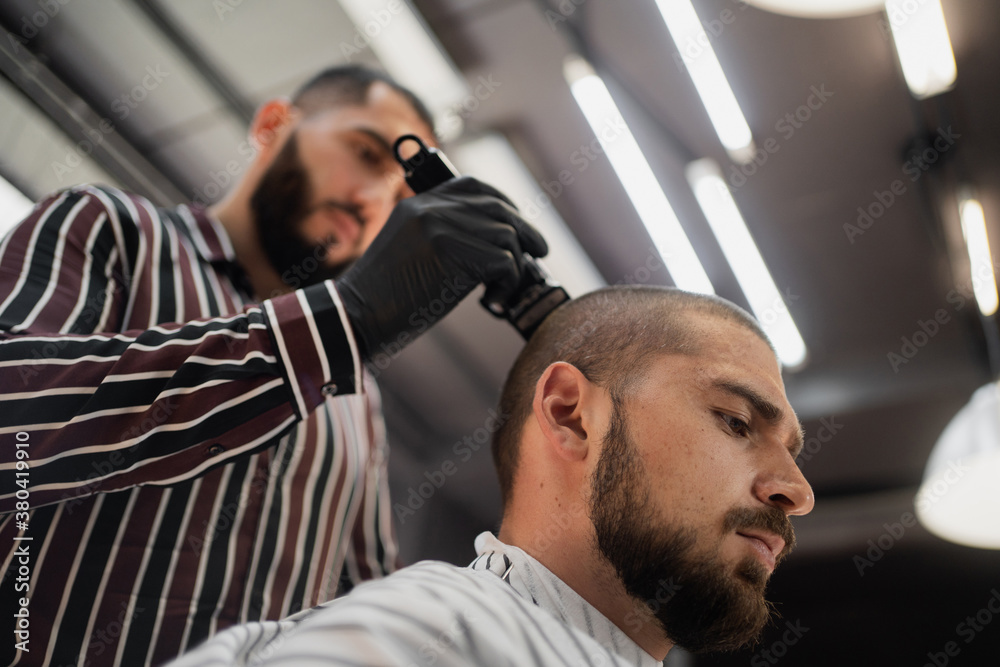 confident young man of brutal Caucasian appearance, doing a haircut of his beard and hair on his head. stylish hair salon and professional master confident young man of brutal Caucasian appearance, doing a haircut of his beard and hair on his head. stylish hair salon and professional master