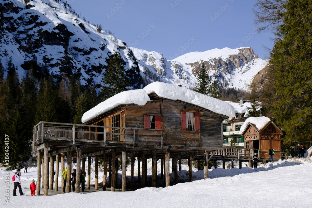 Winter mountain landscape with lake Lago di Braies, wooden pier and silhouettes of tourists, Alta Pusteria, Dolomites, Italy