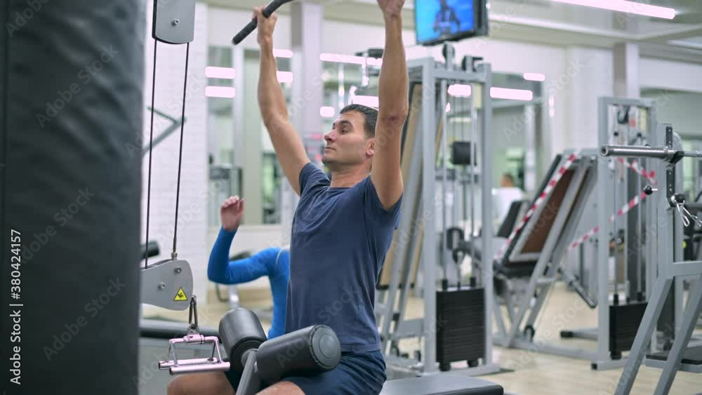 Side view of a woman trainer at a sports club who helps a young man to exercise on an exercise machine Side view of a woman trainer at a sports club who helps a young man to exercise on an exercise machine