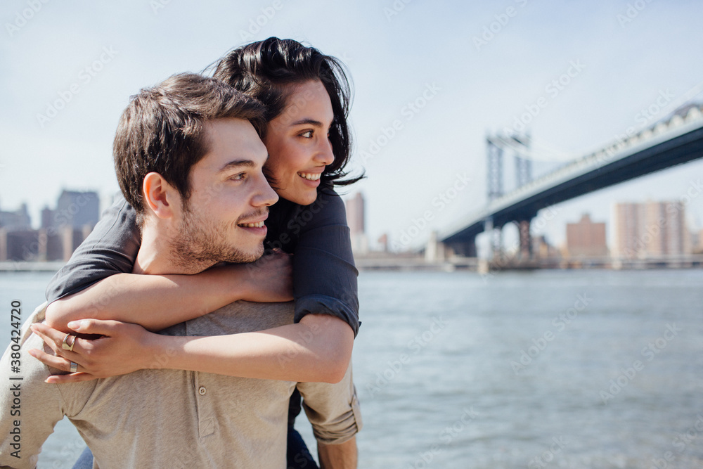 Smiling young couple embracing along the river in Brooklyn, New York Smiling young couple embracing along the river in Brooklyn, New York