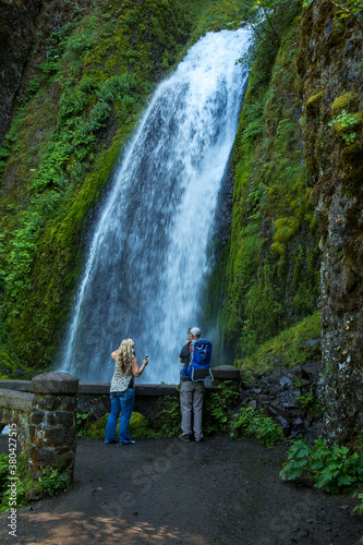 Two hikers aretaking photos of Wahkeena falls  located in the Columbia River Gorge National Scenic Area.
