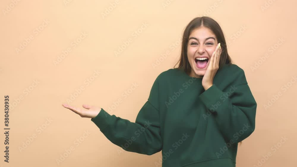 Young caucasian woman holds copy space on a palm, keep hand over cheek amazed and delighted Young caucasian woman holds copy space on a palm, keep hand over cheek amazed and delighted