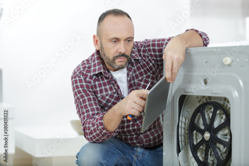 serviceman holding tablet while repairing washing machine