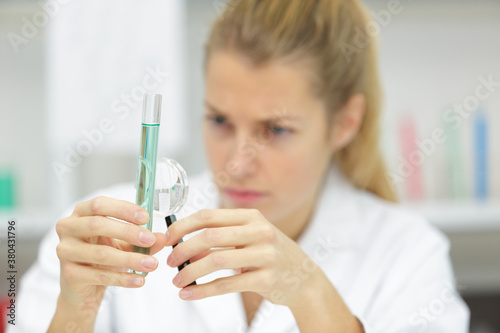 female worker examines the flask with a liquid magnifying glass
