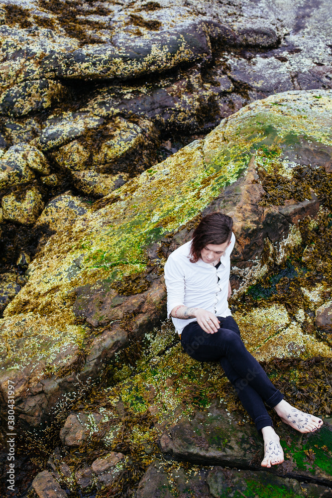 Transgender, gender fluid person hanging out on algae covered rocks at the beach. Transgender, gender fluid person hanging out on algae covered rocks at the beach.